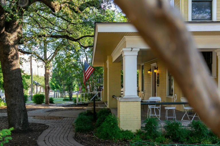 Yellow house with a porch, american flag, and brick pathway