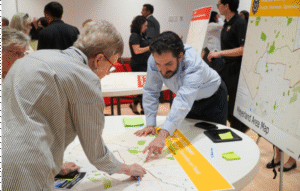 man in blue shirt and older woman with short hair wearing glasses looking and pointing to a point on a map