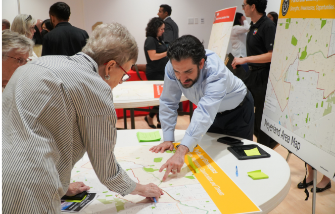 man in blue shirt and older woman with short hair wearing glasses looking and pointing to a point on a map