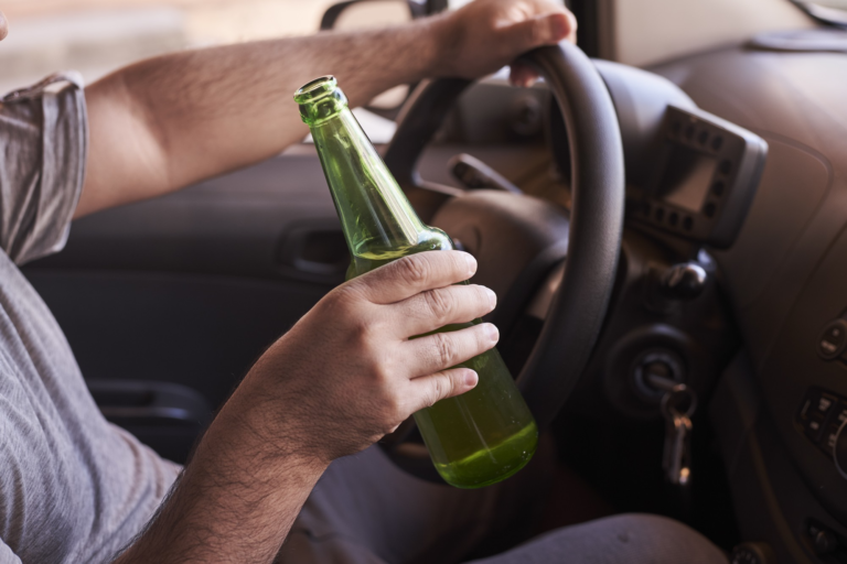 man with a bottle of beer in his hand while driving